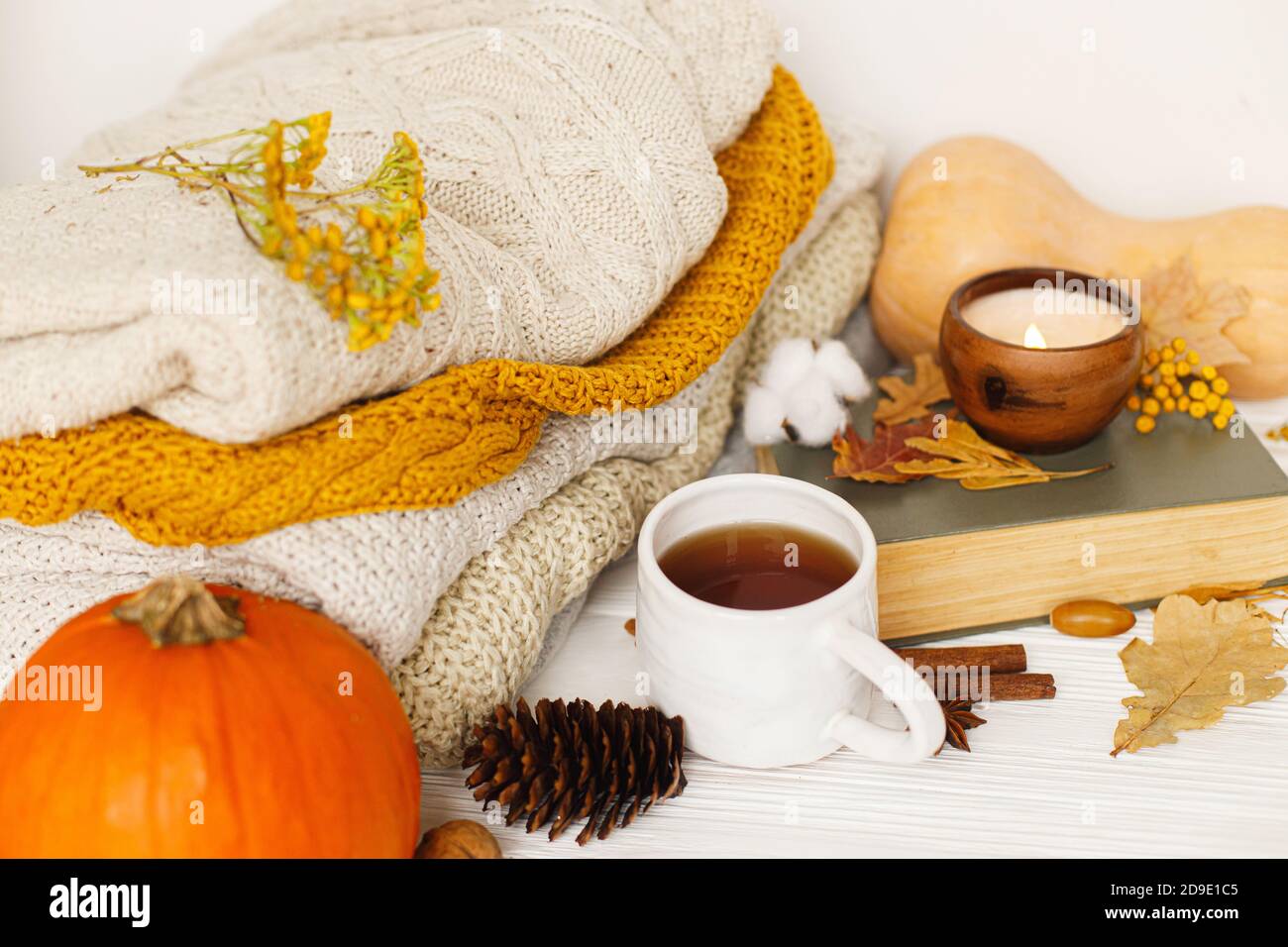 Happy Thanksgiving and Hello fall concept. Warm tea, pumpkins and spices on background of cozy knitted sweaters, autumn leaves, candle and book. Leisu Stock Photo