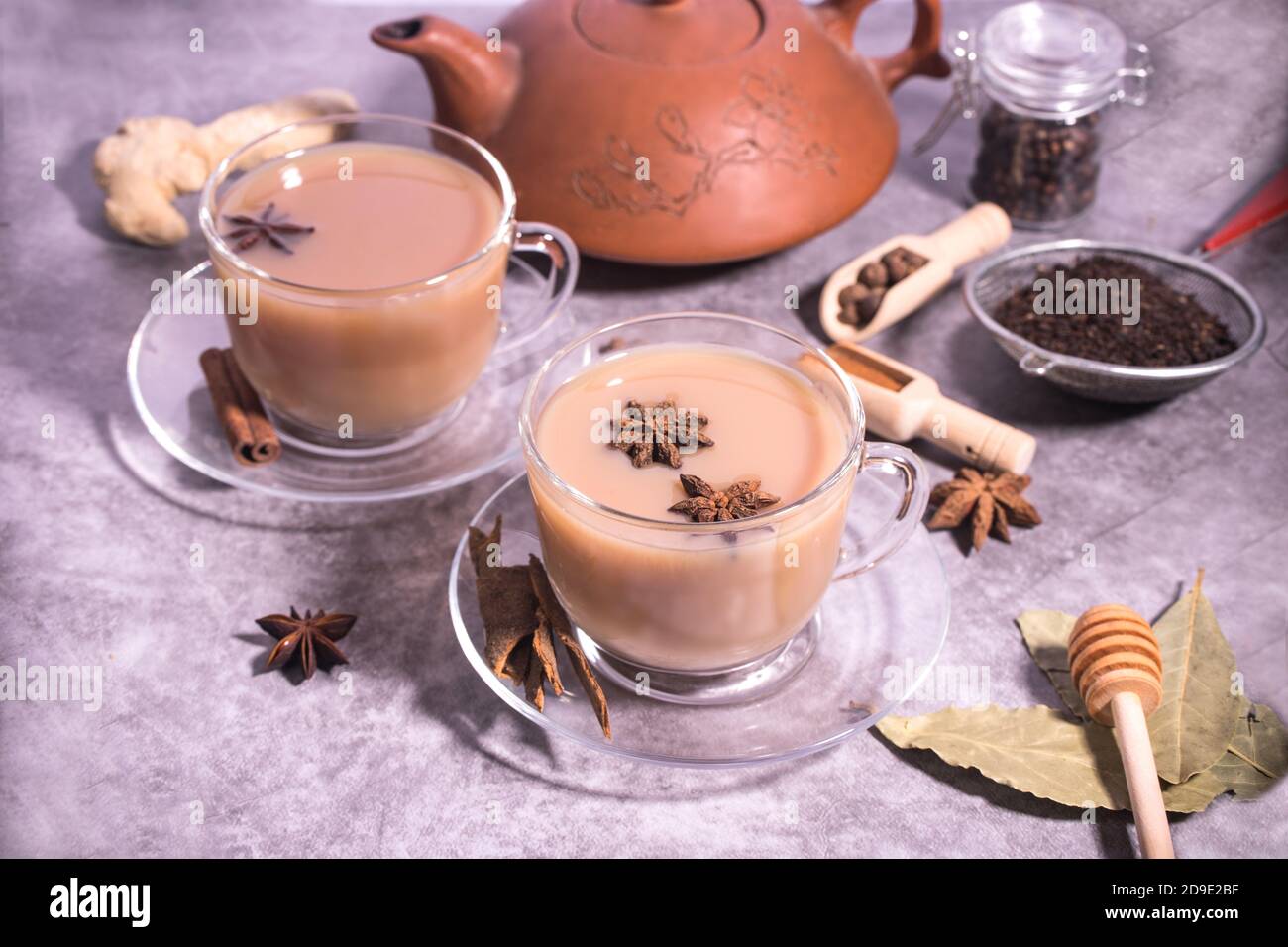 Masala tea-Indian invigorating tea with milk and spices on a gray background in cups and teapot. Horizontal orientation. Stock Photo