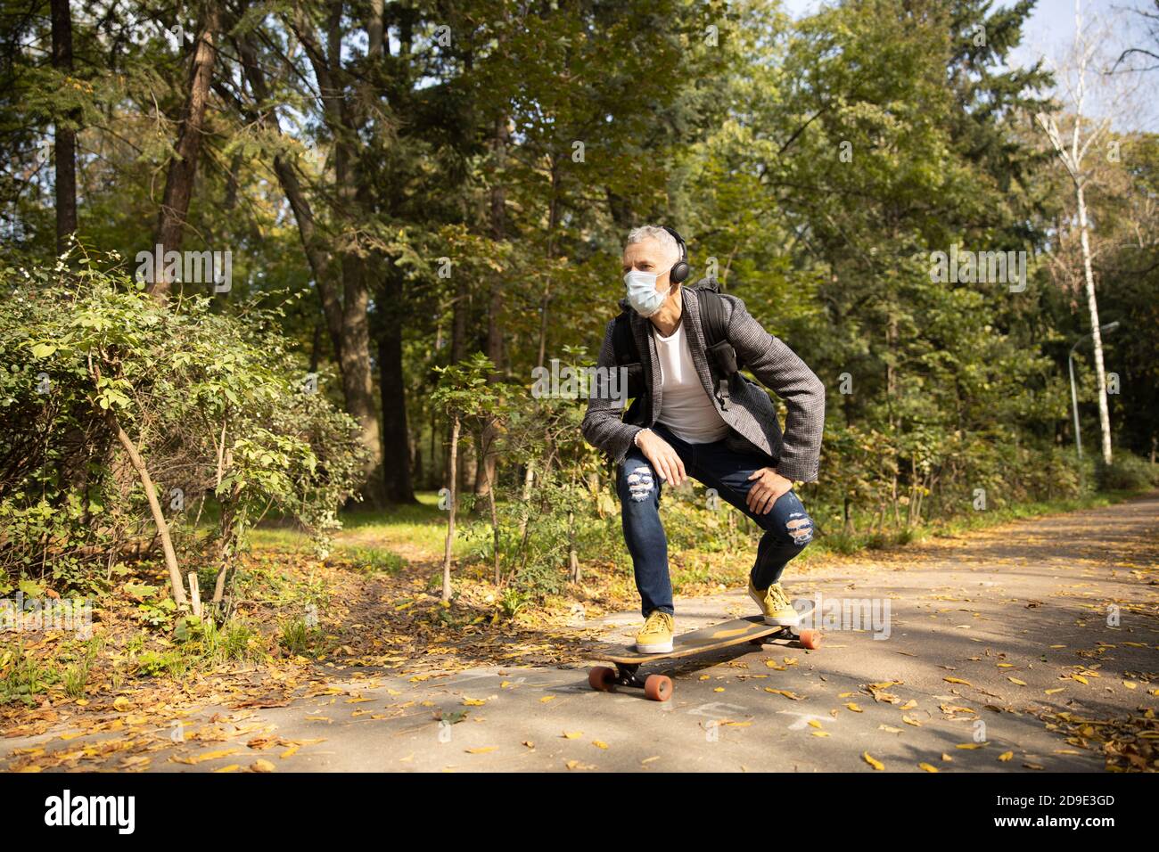Athletic man in mask going skateboarding in park Stock Photo