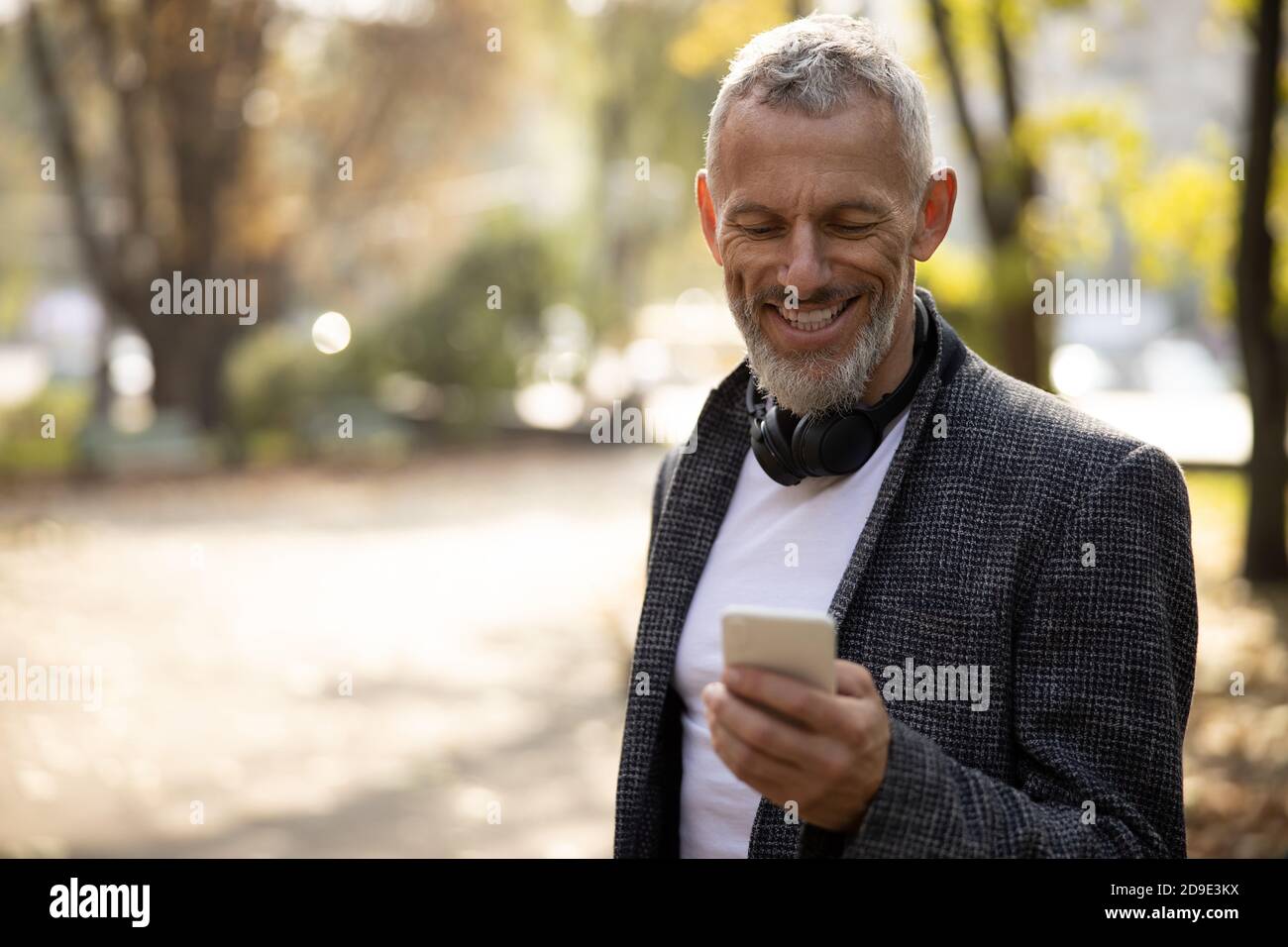 Cheerful handsome man standing outdoors and using smartphone Stock Photo