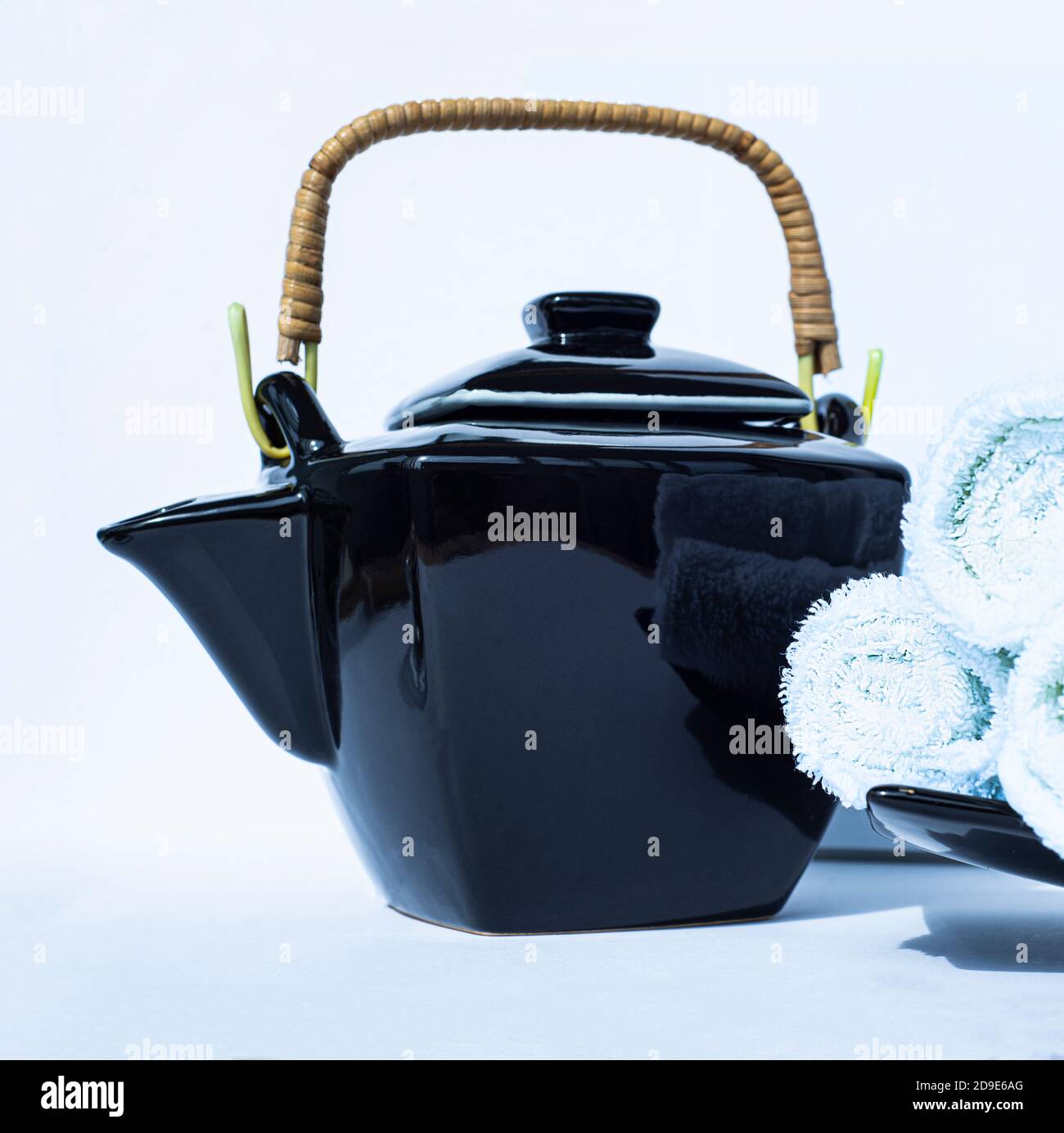 Black teapot with a wicker handle in oriental style and rolls of white terry towels on a white