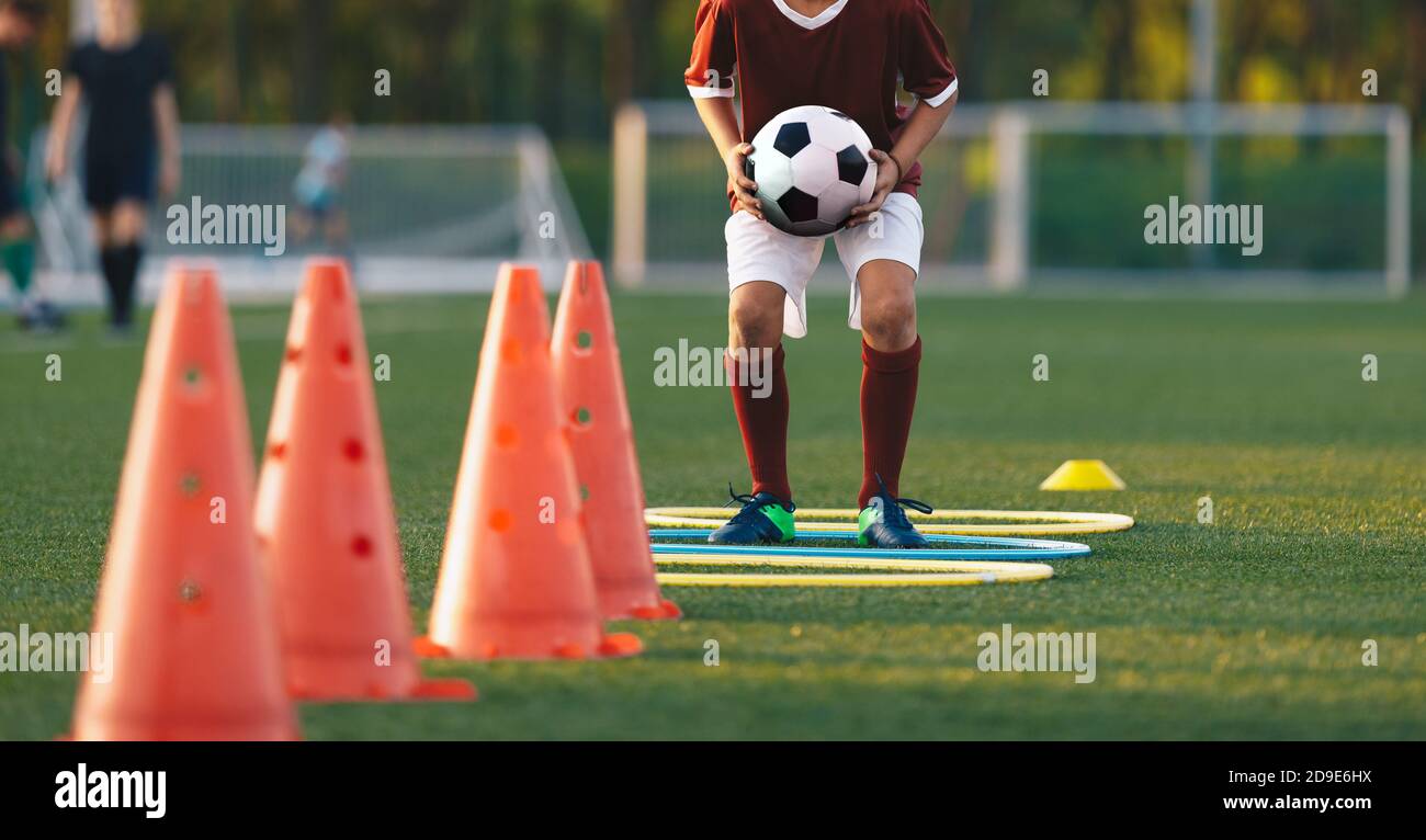Close up boy running on football training pitch with ball in his hands. Player jumping over obstacles. Football training obstacle course. Children lev Stock Photo