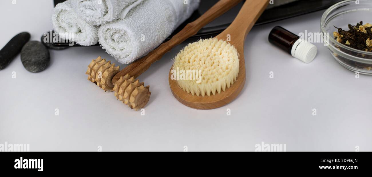 SPA Background for a banner with wellness items. Brush for dry body massage. Wooden massager for face and body. Wet white towels on a ceramic dish.  Stock Photo