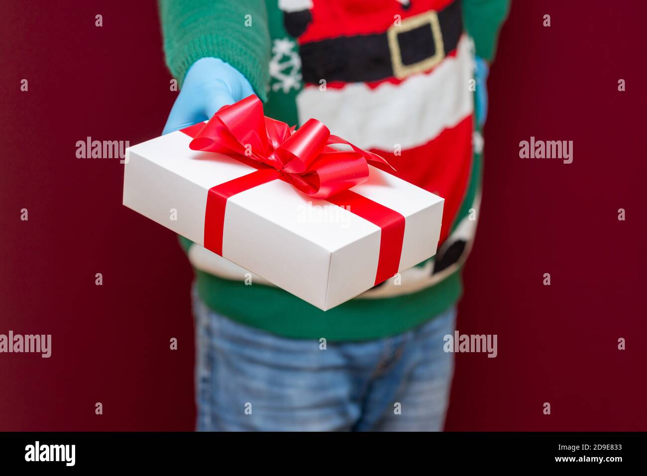 Close up cropped shot of male hands holding white gift box on red studio background.Christmas concept. Stock Photo