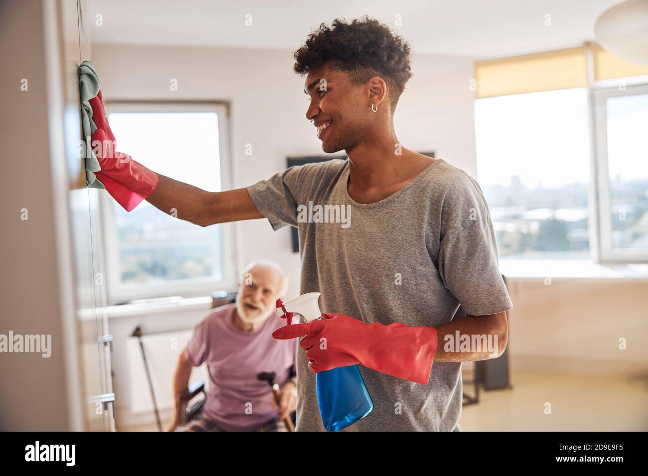 Smiling volunteer cleaning the room of a senior man Stock Photo Alamy