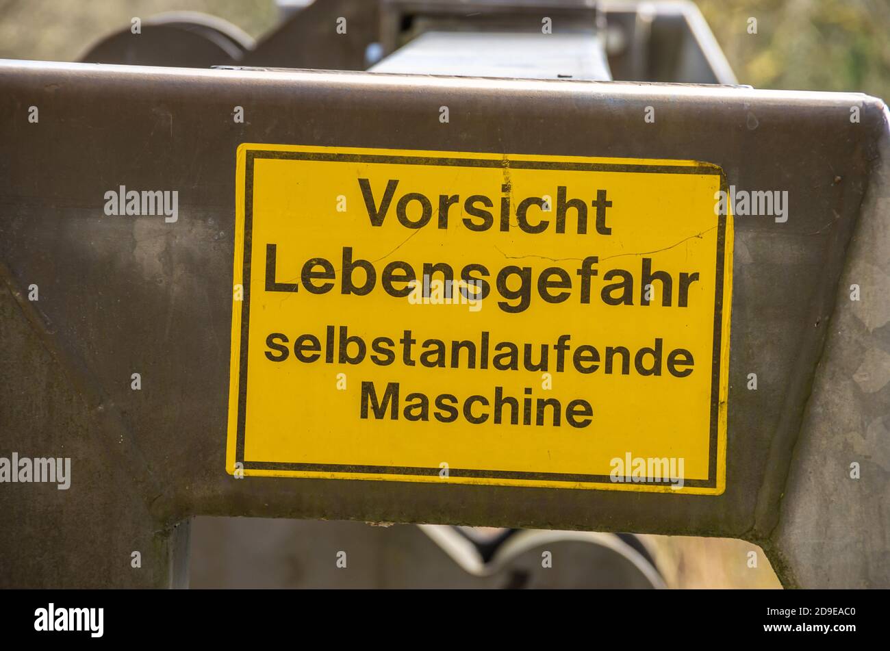 German warning sign - Vorsicht Lebensgefahr selbstanlaufende Maschine at a mechanism. Stock Photo