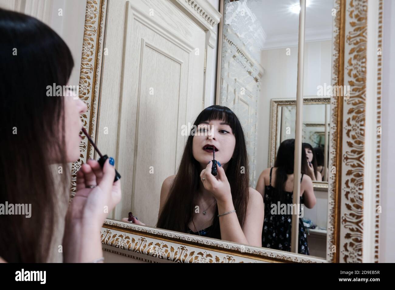Young woman applying lipstick in front of a mirror. Girl getting ready with her makeup in a hotel bathroom. Pretty female painting lips Stock Photo