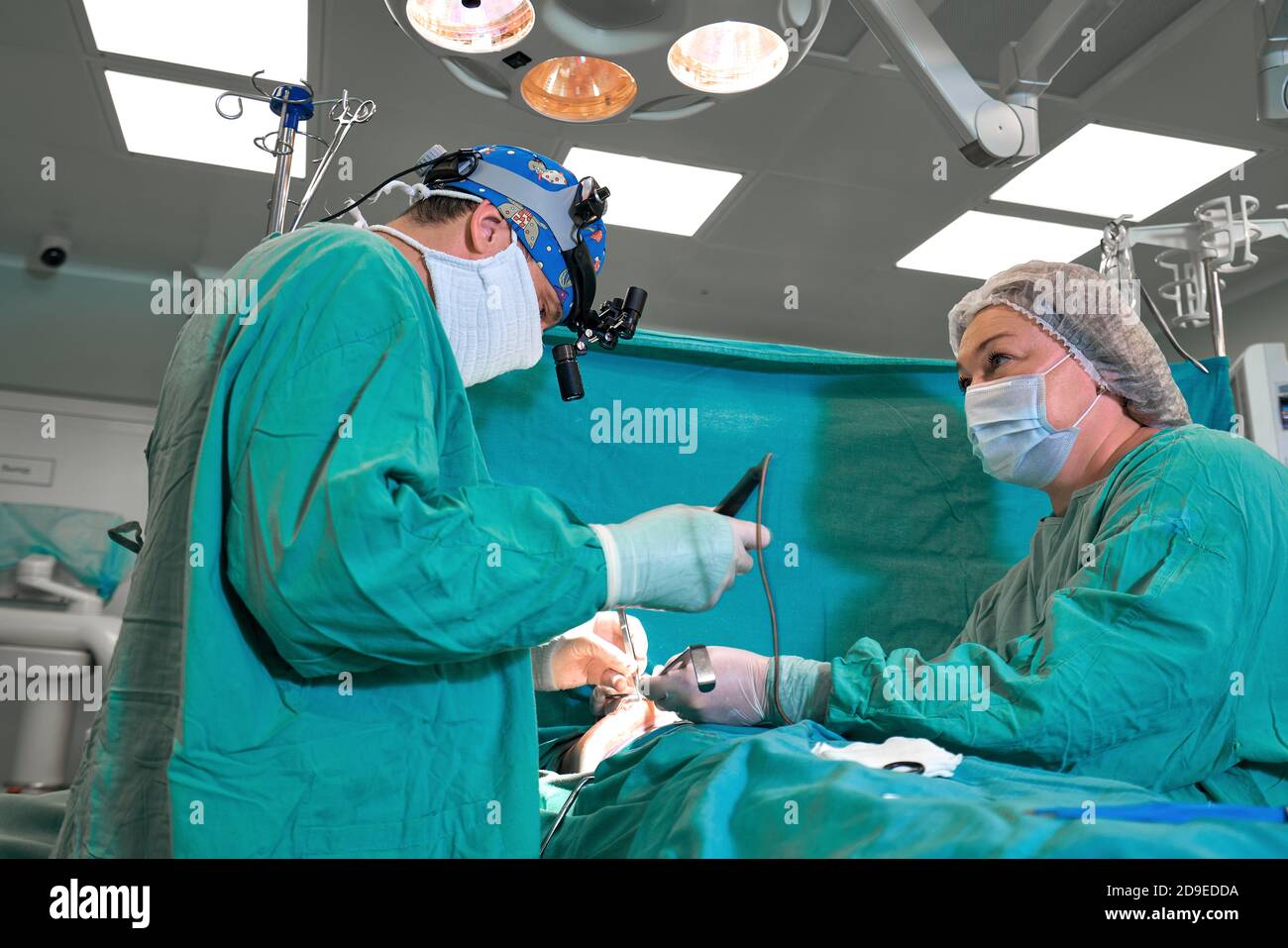 Surgeon and his assistant performing cosmetic surgery on nose in hospital operating room. Nose reshaping, augmentation. Rhinoplasty. Stock Photo