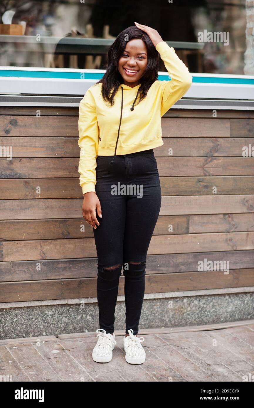 Hipster african american girl wearing yellow hoodie posing at street  against wooden house with windows Stock Photo - Alamy