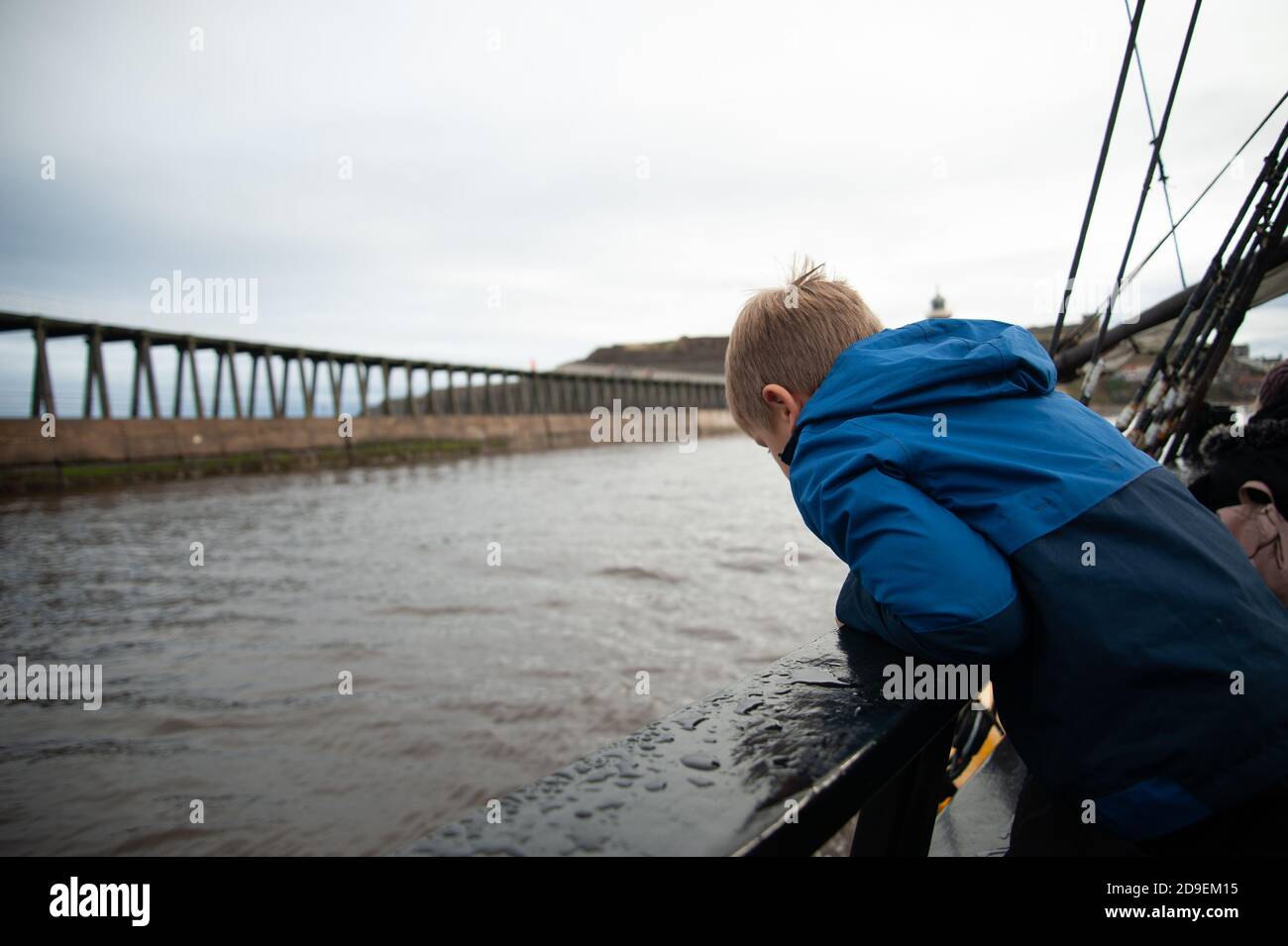 A young boy looks at the east pier from the deck of a replica of Captain Cooks Endeavour, Whitby Harbour, Whitby, Yorkshire, England. Stock Photo