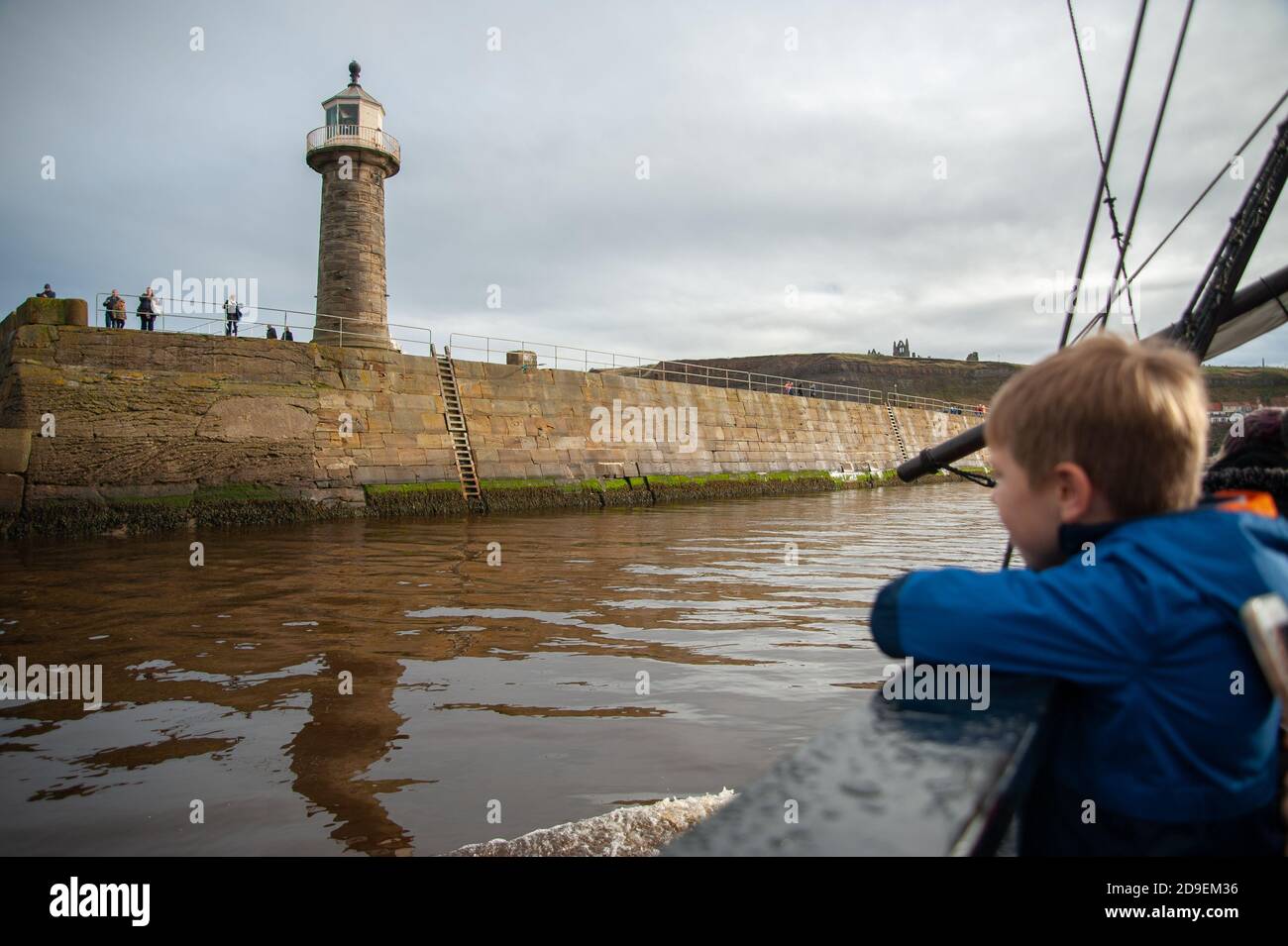 A young boy looks at the east pier from the deck of a replica of Captain Cooks Endeavour, Whitby Harbour, Whitby, Yorkshire, England. Stock Photo