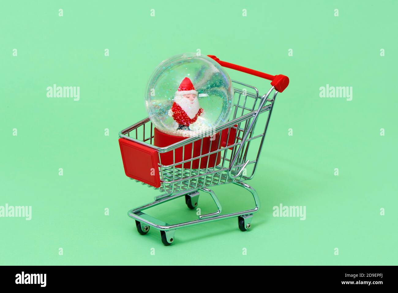a christmas snow globe, with a santa claus inside, in a shopping cart on a green background Stock Photo