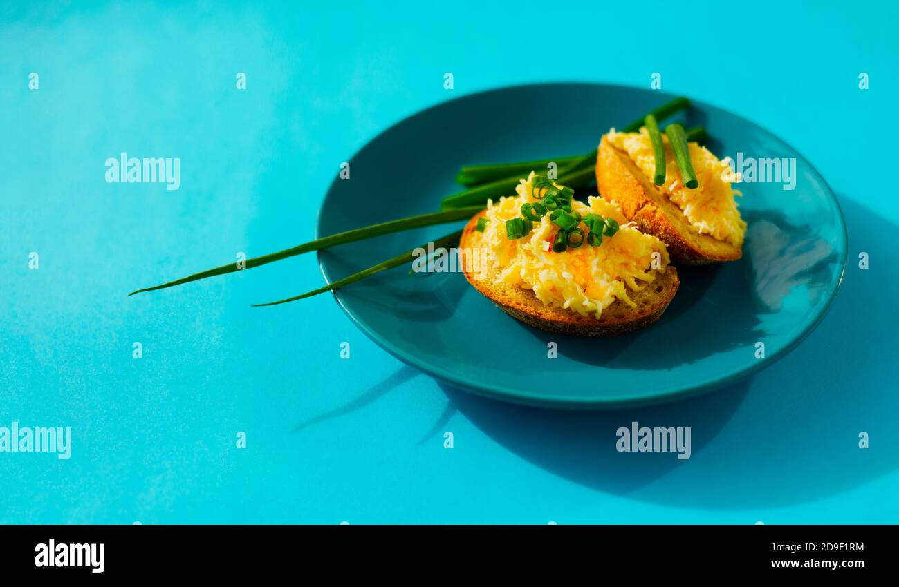 Two sandwiches with Jewish appetizer and green onions on a turquoise plate on a turquoise background. Rye bread with grated cheese.  Stock Photo