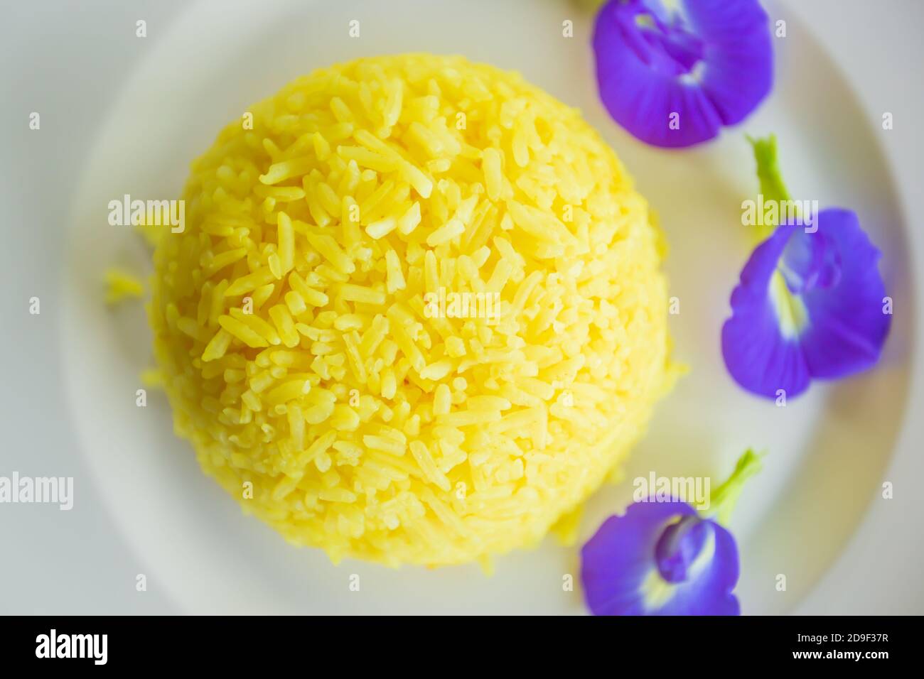 Turmeric Rice with Butterfly pea flowers on white plate, tasty yellow steamed rice with purple flowers on white plate. Flat lay. Top view. Close-up. Stock Photo