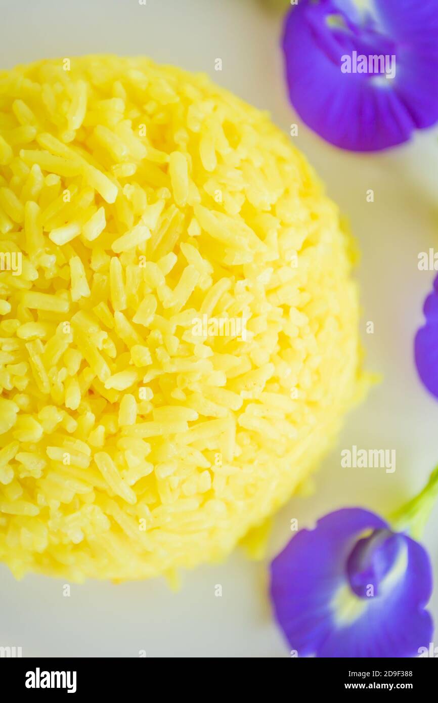 Turmeric Rice with Butterfly pea flowers on white plate, tasty yellow steamed rice with purple flowers on white plate. Flat lay. Top view. Close-up. Stock Photo