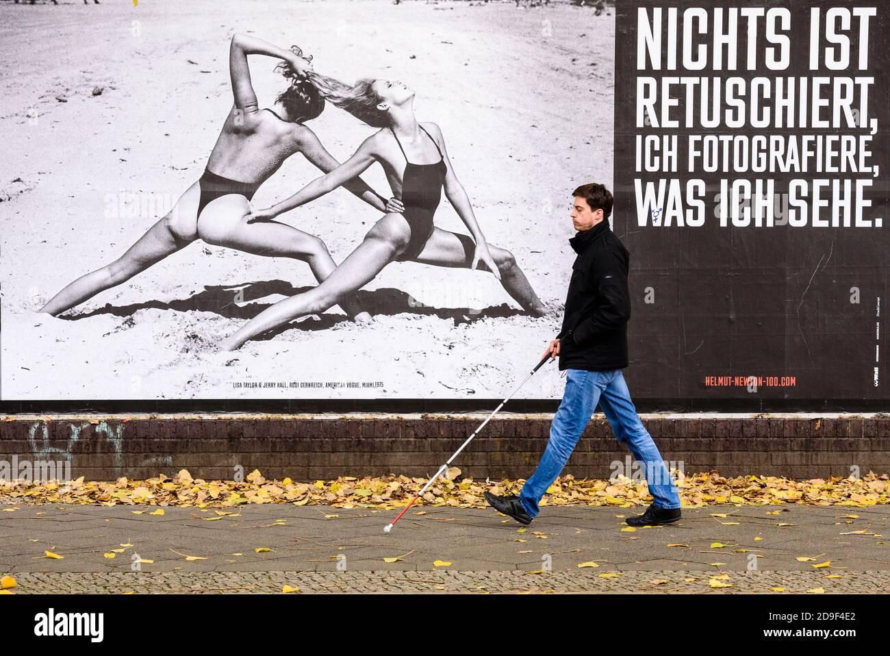 Germany, Berlin, November 05, 2020: A man with a cane for the blind walks in front of a large black and white photograph by fashion photographer Hetmut Newton next to a lettering reading 'Nothing is retouched, I photograph what I see' (German: 'Nicht ist retuschiert, ich fotografie was ich sehe'). On the occasion of the 100th birthday of German-Australian photographer Helmut Newton (born Helmut Neustaedter), the Helmut Newton Foundation is presenting the exhibition 'Helmut Newton One Hundred' with 30 selected works from October 31 to November 8, 2020. The photo exhibition covers the 85 meter l Stock Photo