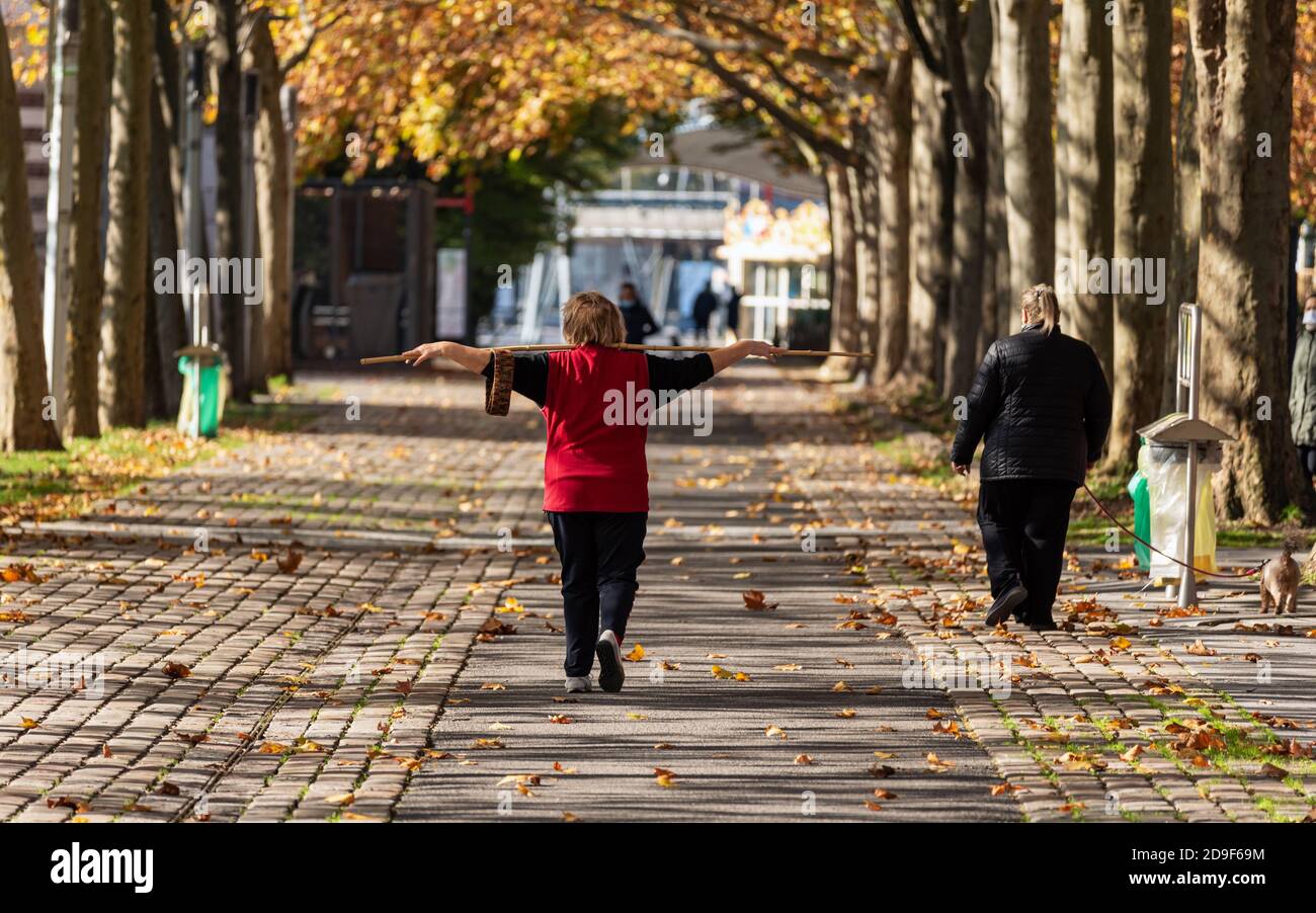 People walking in a parisian park during lockdown in Autumn. A woman is doing stretching exercises with a stick while another is walking her dog. Stock Photo