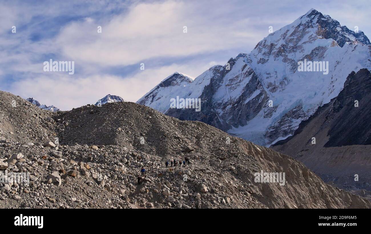 People hiking through the rock-covered majestic Khumbu glacier on the way to village Gorakshep on Everest Base Camp Trek with snow-capped Nuptse. Stock Photo