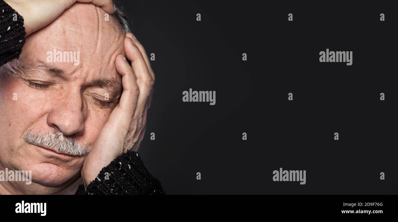an older man suffering from a headache on dark background Stock Photo