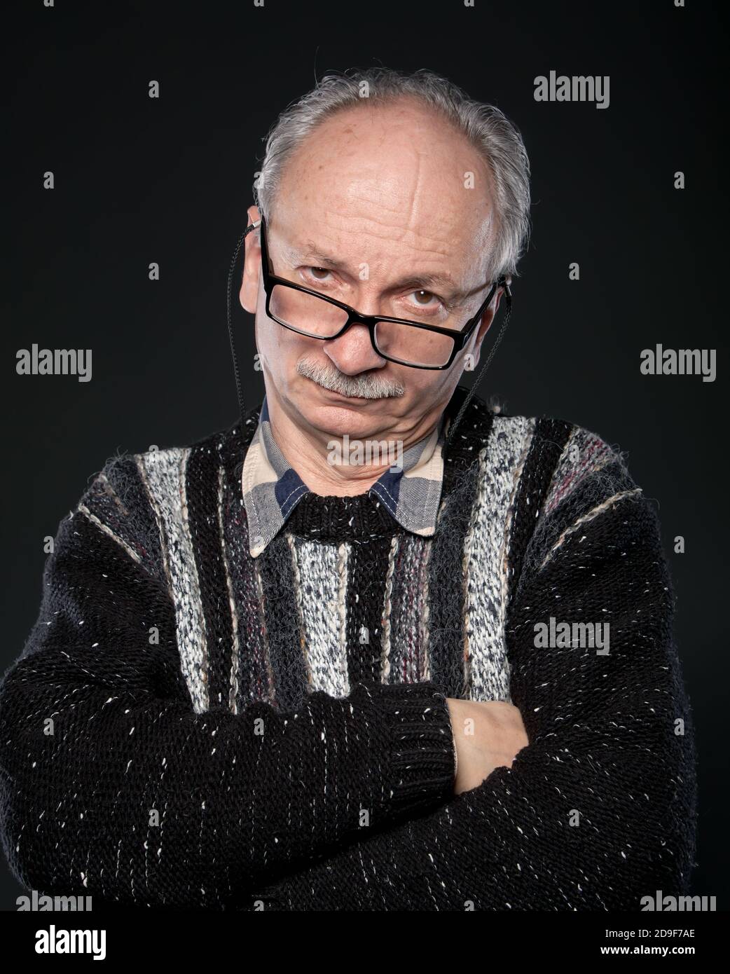 An elderly man with glasses and crossed arms looks skeptically on a ...