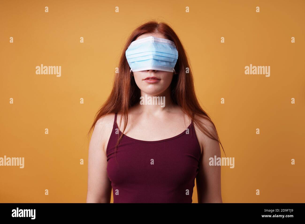 young woman wearing medical face mask over her eyes - funny corona denier concept Stock Photo