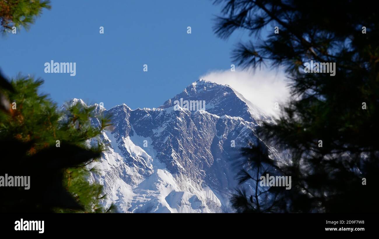 First view of the peak of mighty Mount Everest (summit: 8,848 m) on Everest Base Camp Trek through a gap between trees on the ascent to Namche Bazar. Stock Photo