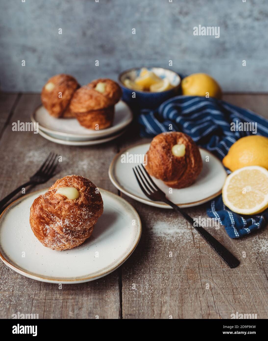 Lemon filled cruffins on wooden table with plates and forks. Stock Photo