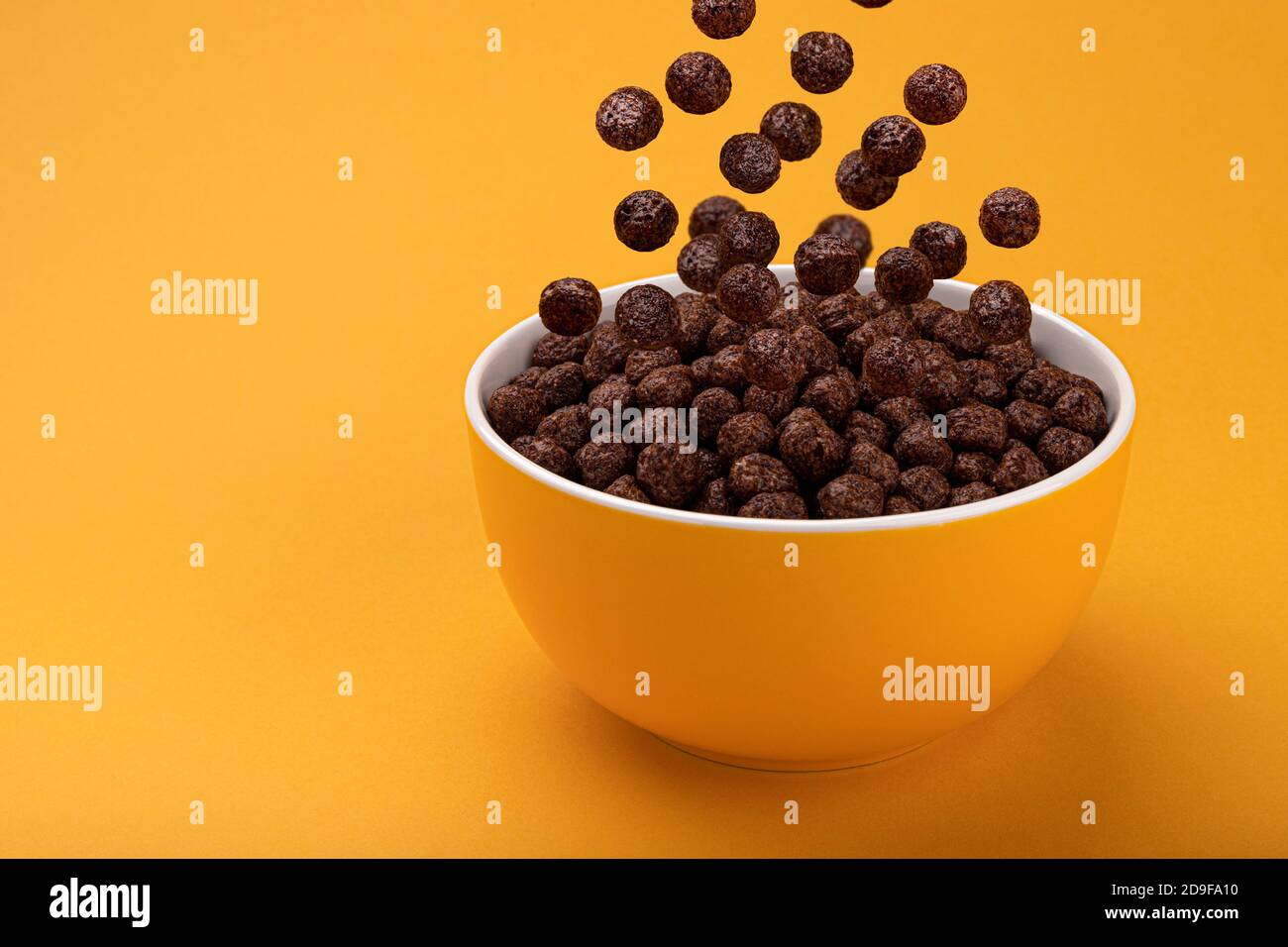 Chocolate Corn balls falling in bowl over yellow background Stock Photo