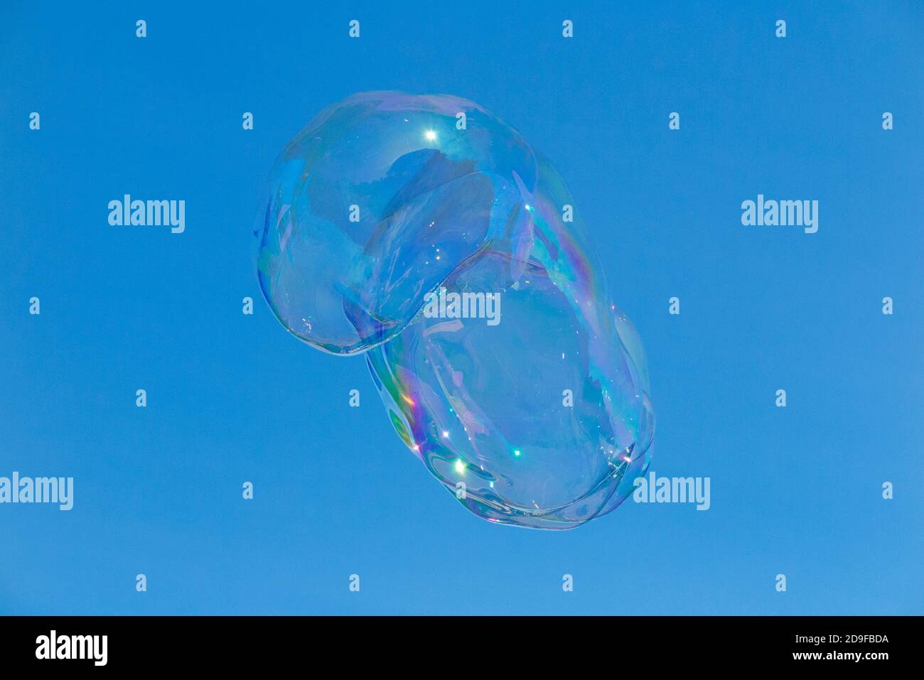Surreal bubbles floating a clear blue sky on a sunny day and glittering in the sun shine. Created by a Bubbleologist at an outdoor event. UK (120) Stock Photo