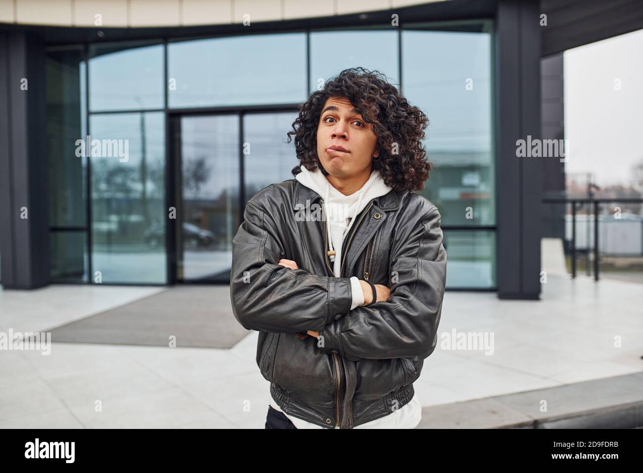 Handsome young man with curly black hair is on the street against building Stock Photo
