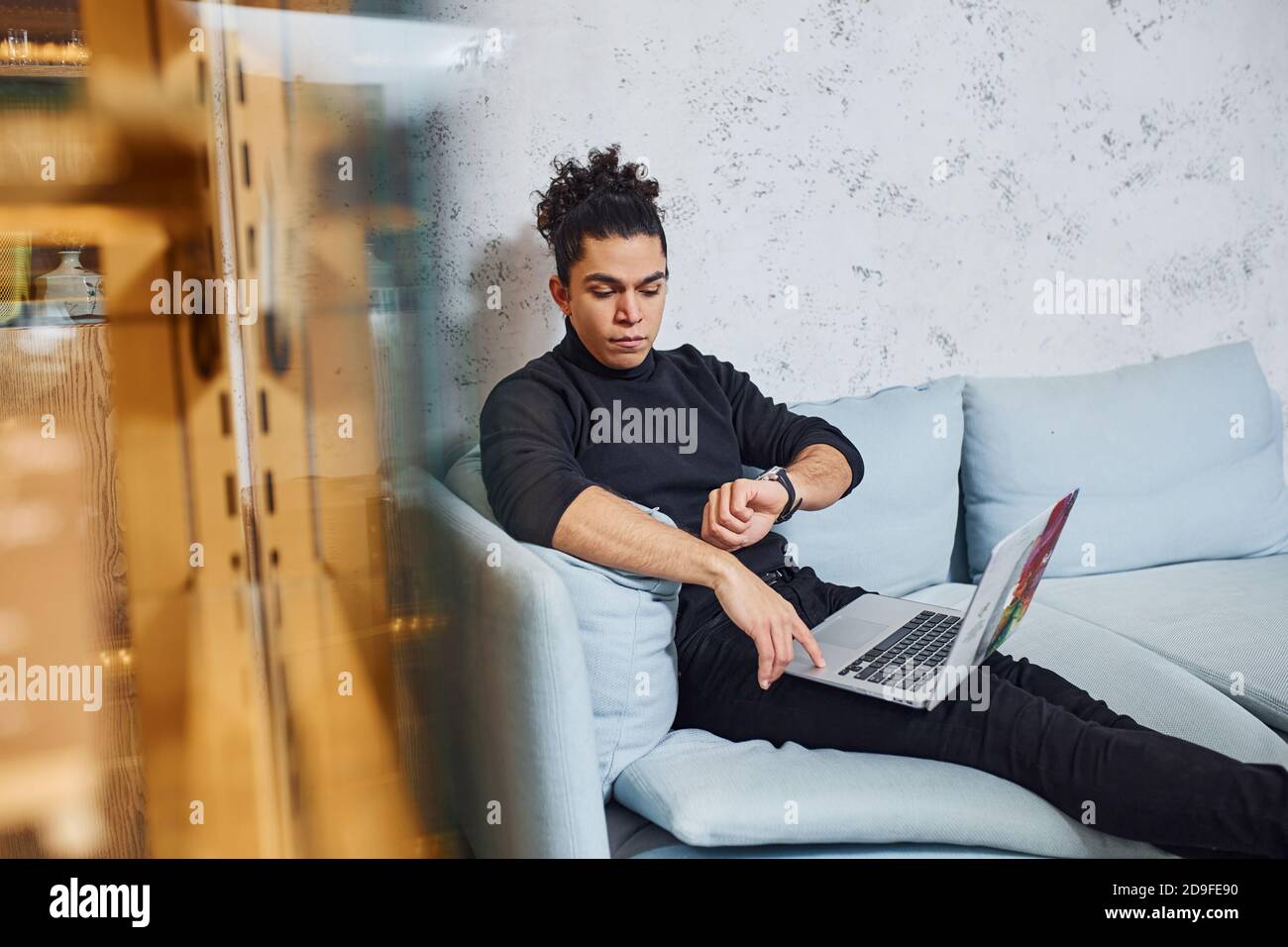 Handsome young man with curly black hair indoors with laptop Stock Photo