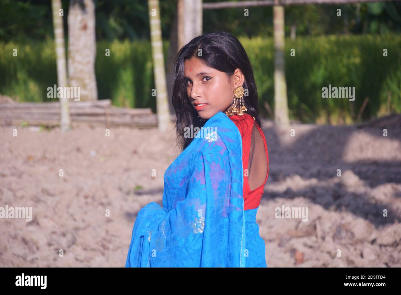 Close up of side face of an Indian teenage girl wearing blue sari with red blouse nose pin big earring standing on a plowed field, selective focusing Stock Photo