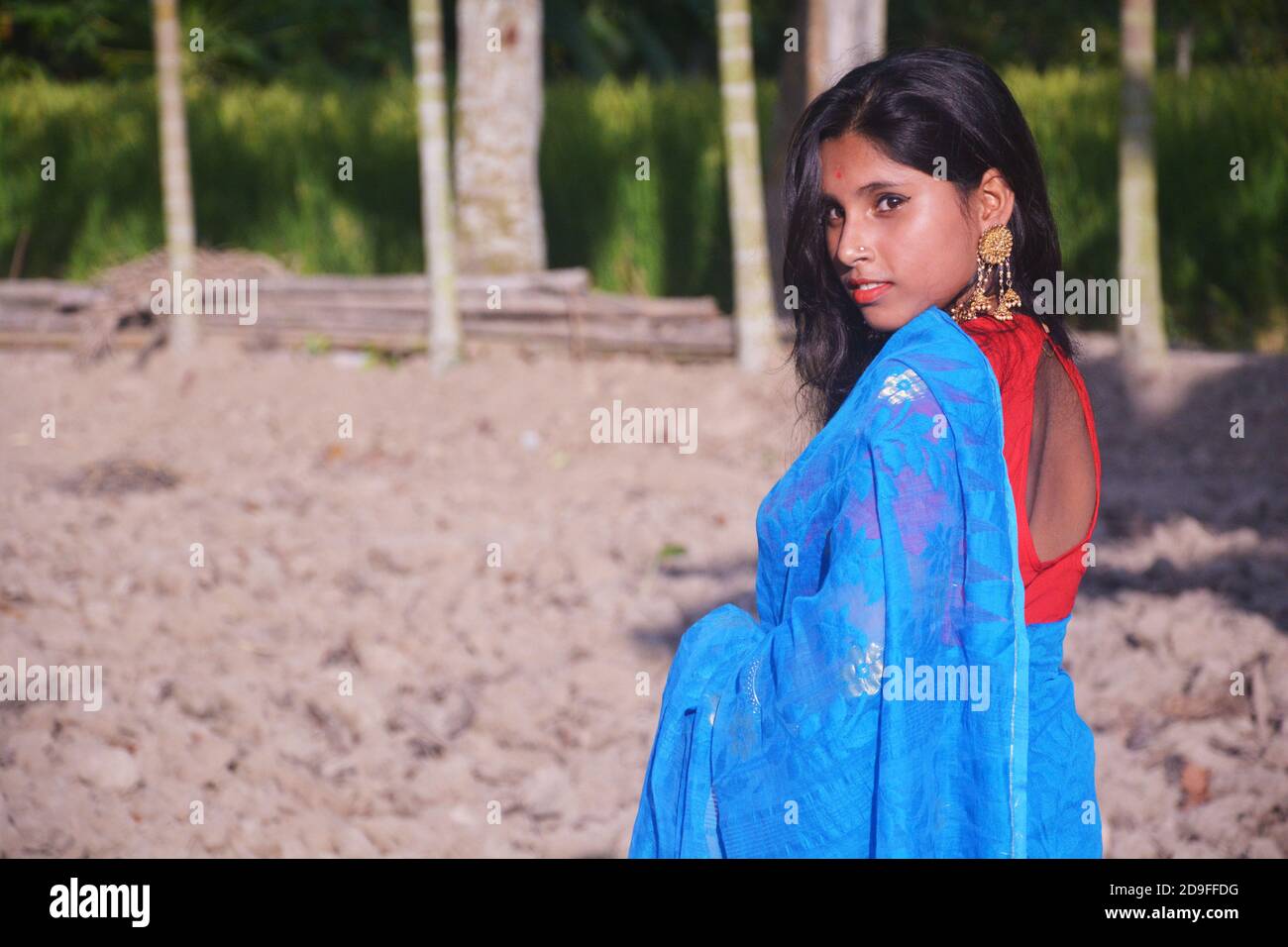 Close up of side face of an Indian teenage girl wearing blue sari with red blouse nose pin big earring standing on a plowed field, selective focusing Stock Photo