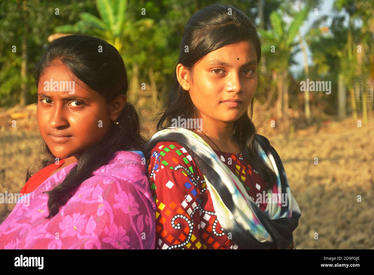 Two beautiful Indian teenage Bengali girls wearing sari salwar kameez and golden jewelleries like earrings nose pin and standing back to back Stock Photo