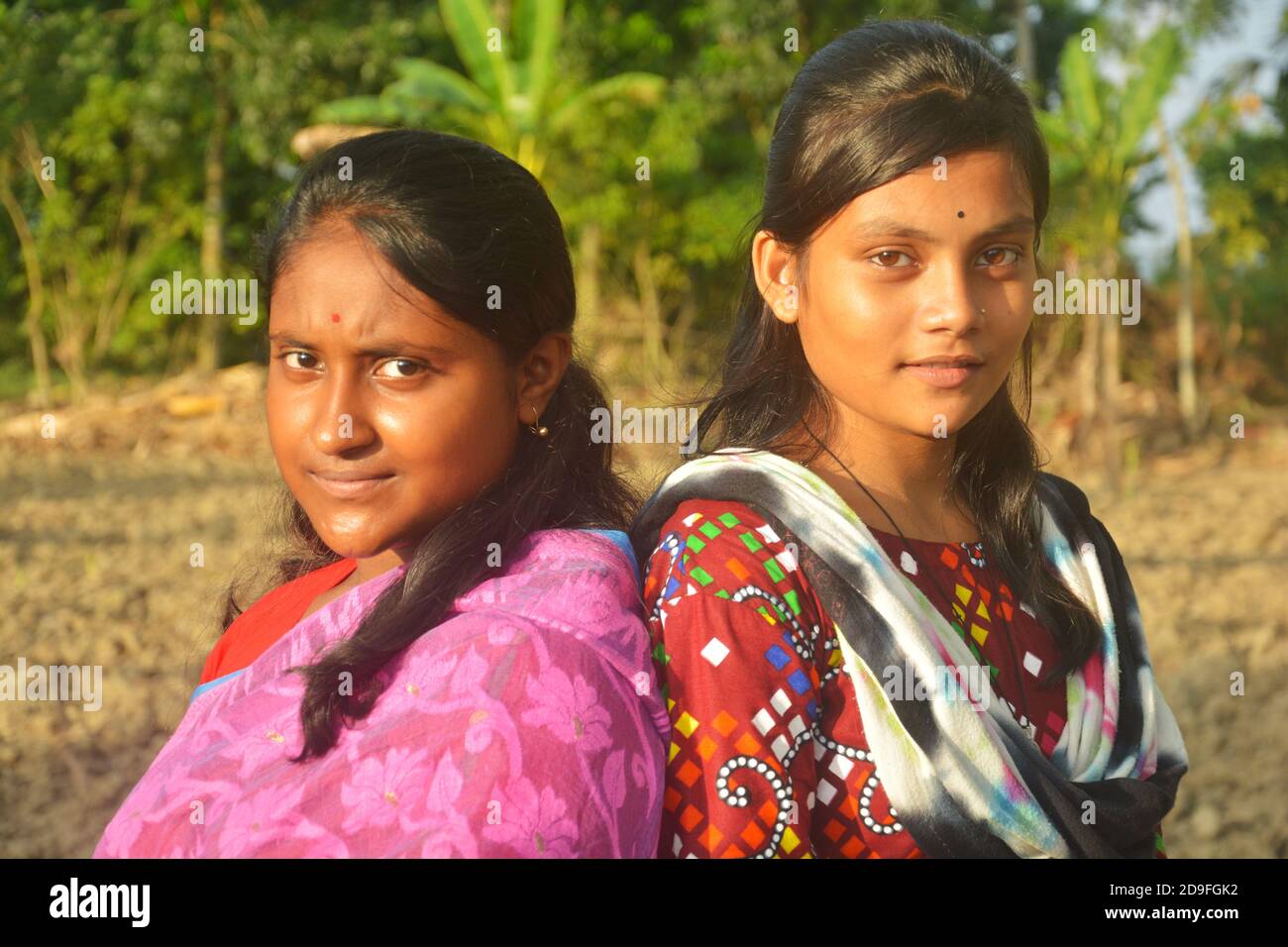 Two beautiful Indian teenage Bengali girls wearing sari salwar kameez and golden jewelleries like earrings nose pin and standing back to back Stock Photo
