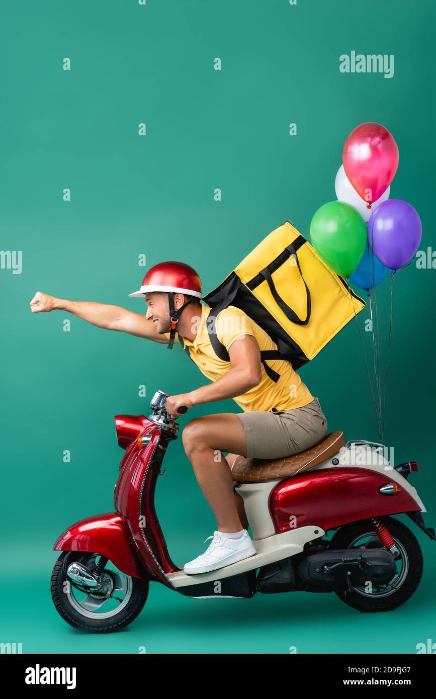 Side View Of Happy Delivery Man With Backpack And Outstretched Hand Riding Scooter With Balloons On Blue Stock Photo Alamy Side View Of Happy Delivery Man With Backpack And Outstretched Hand Riding Scooter With Balloons On Blue Stock Photo Alamy