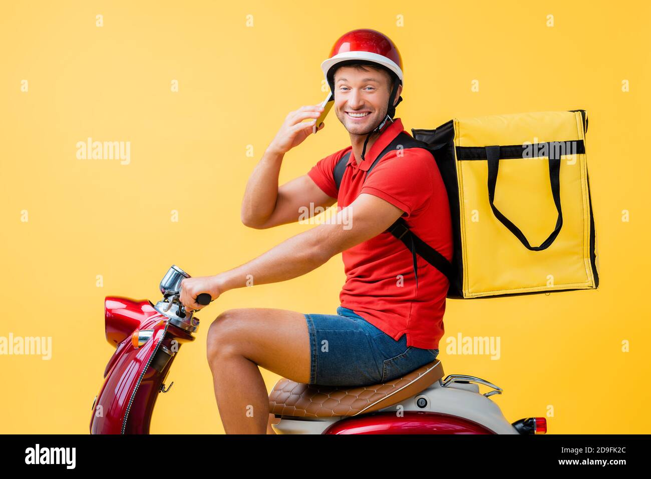 happy delivery man in helmet and backpack riding red scooter while ...