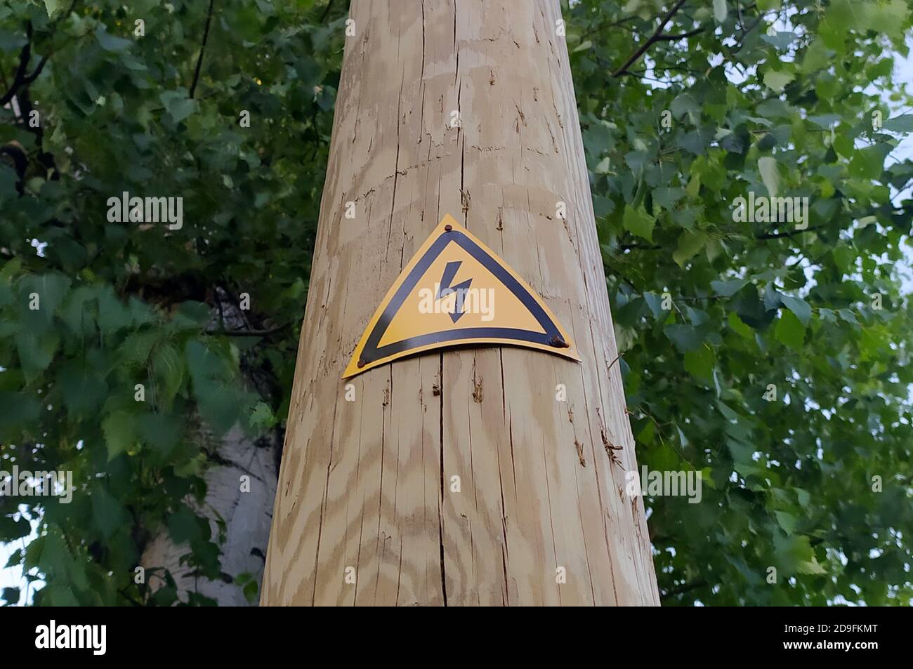 Sign of danger of electric shock on a wooden pole. Black lightning against a yellow triangle. Stock photo with empty space for text and design. Stock Photo