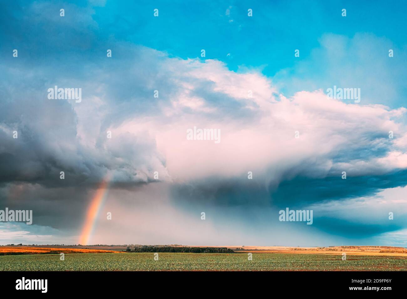 Dramatic Sky During Rain With Rainbow On Horizon Above Rural Landscape