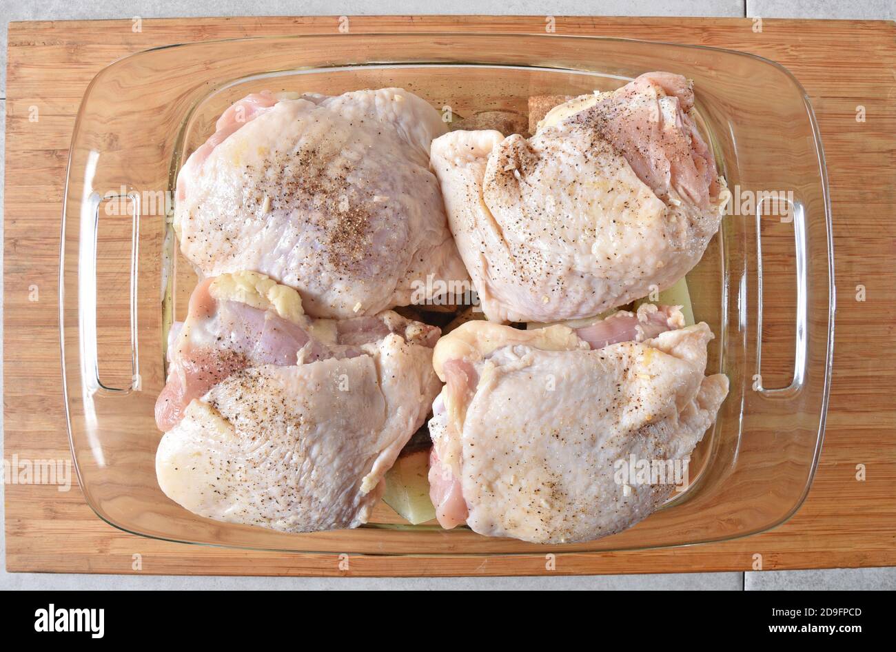 Overhead view of raw chicken thighs on top of diced potatoes in a baking dish Stock Photo