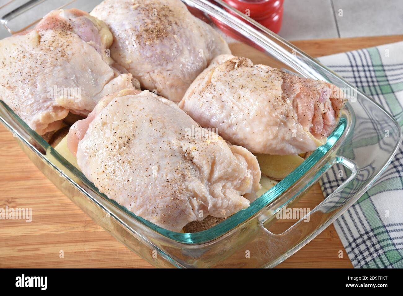 Chicken thighs in a baking pan on top of a layer of diced potatoes ready for the oven Stock Photo