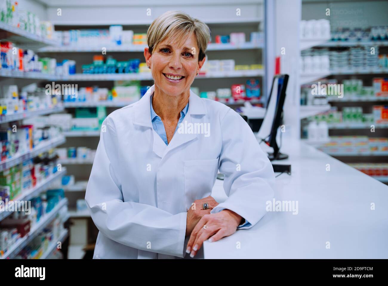 Portrait of smiling caucasian pharmacist leaning against prescription counter in pharmacy Stock Photo