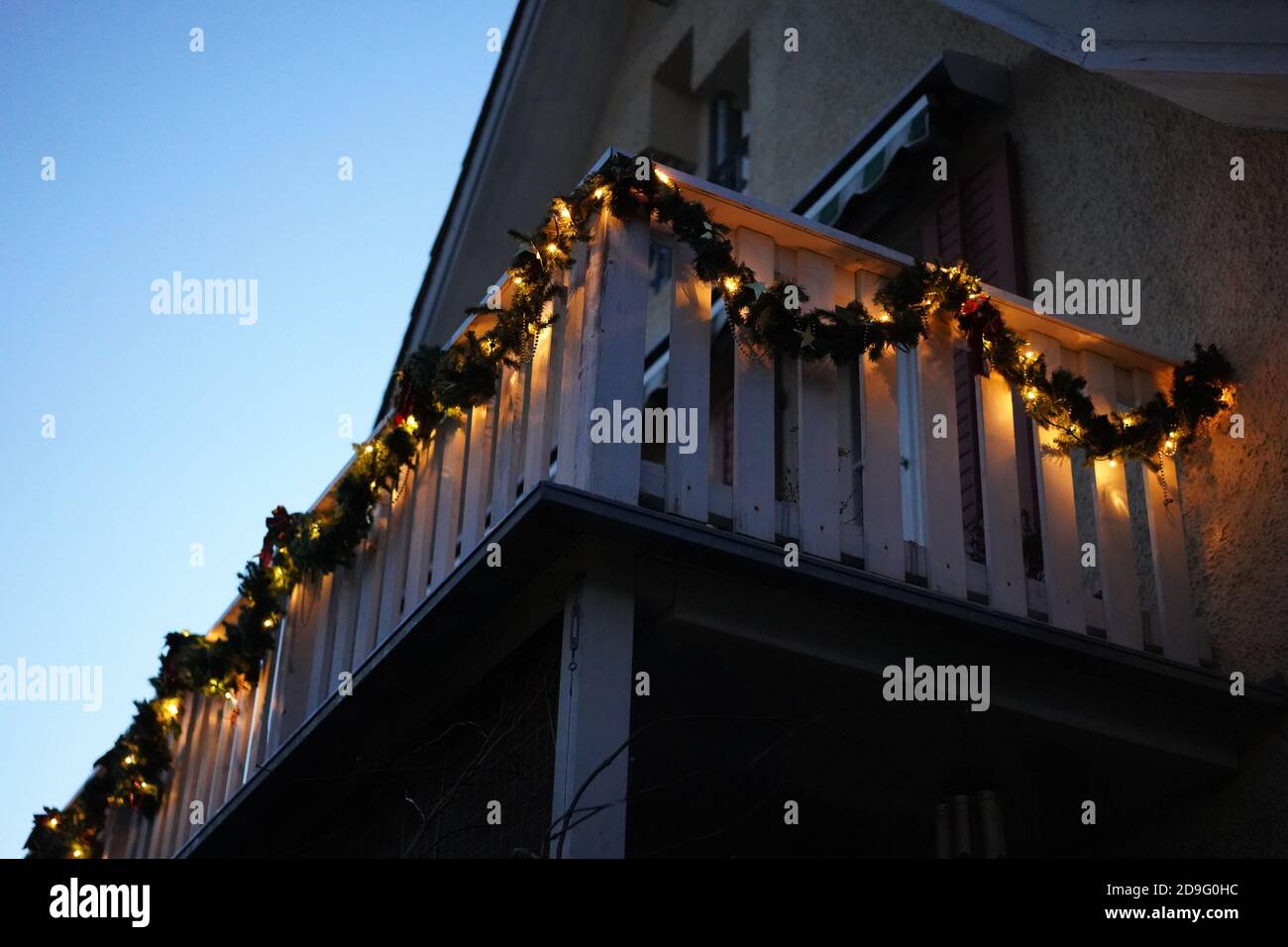 Christmas wreaths with candle lights on wooden balcony in the dusk at Christmastime. Tree at left side with space in the middle. Low angle view. Stock Photo