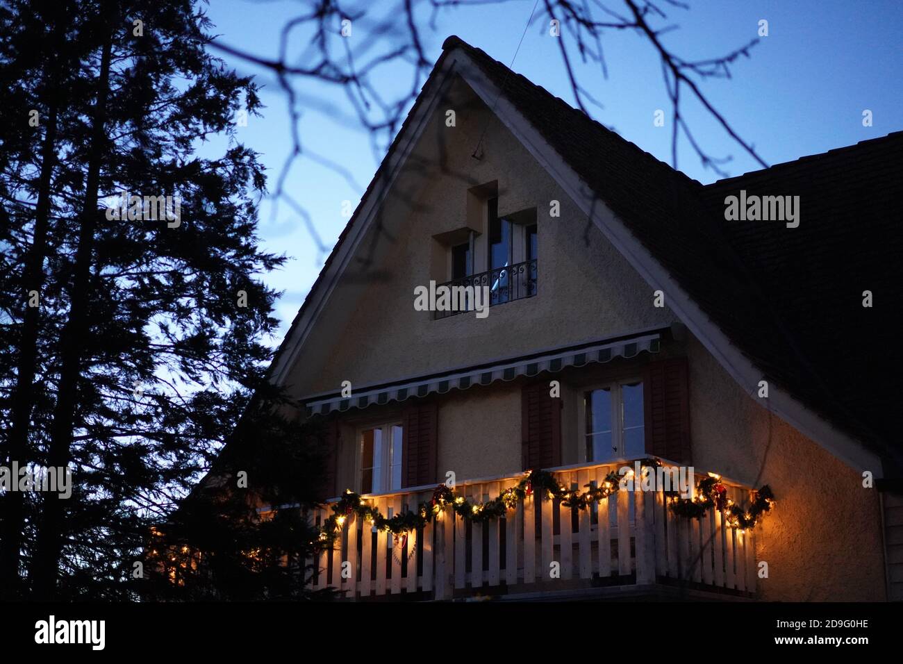 Christmas wreaths with candle lights on wooden balcony in the dusk at Christmastime. Tree at left side with space in the middle. Low angle view. Stock Photo