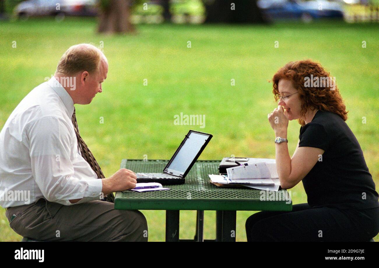 Business man on laptop works with secretary at picnic table in a public park Stock Photo
