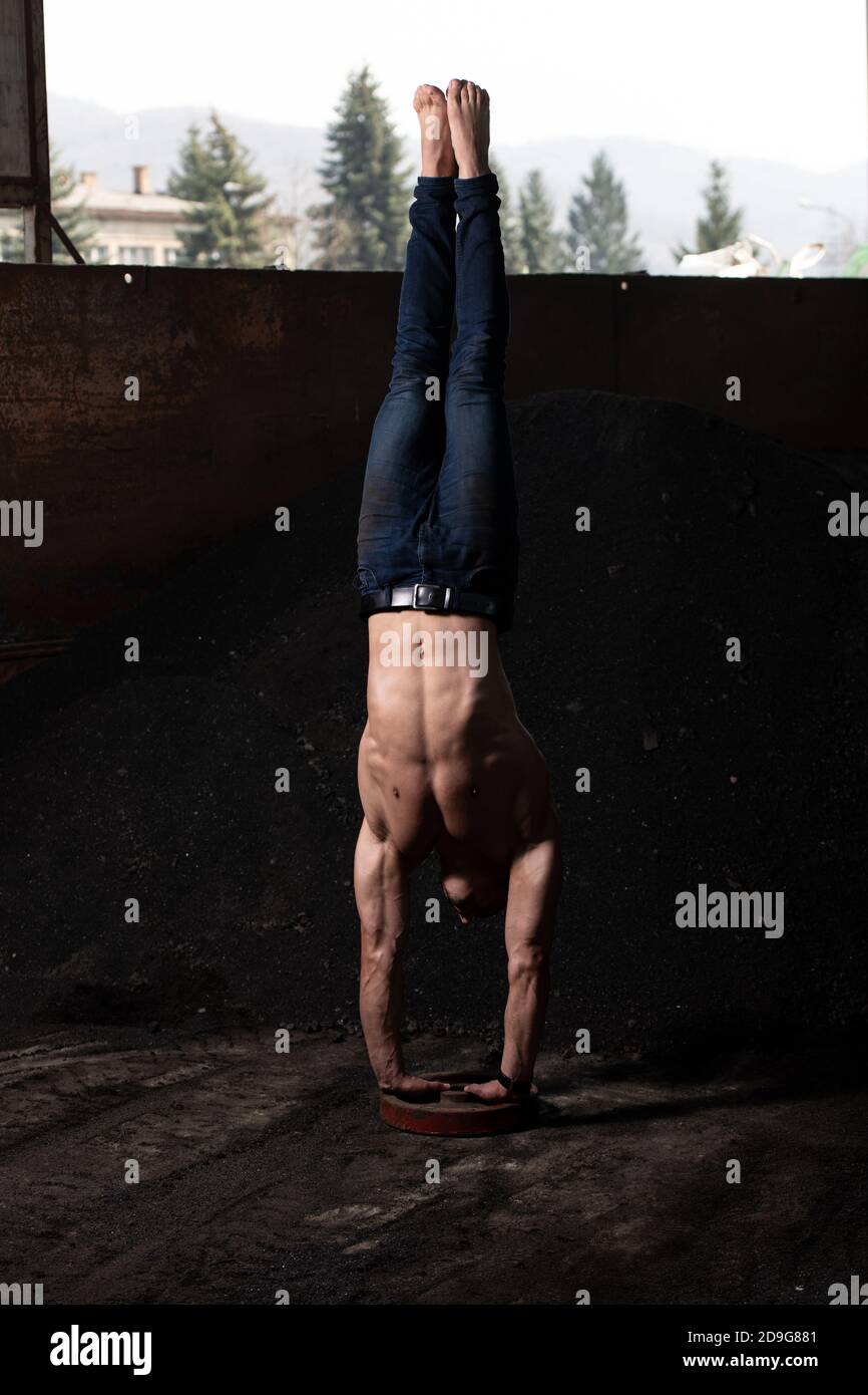 Young Man Keeping Balance on Hands in Warehouse - Muscular Athletic Bodybuilder Fitness Model Doing Handstand Push-up Stock Photo