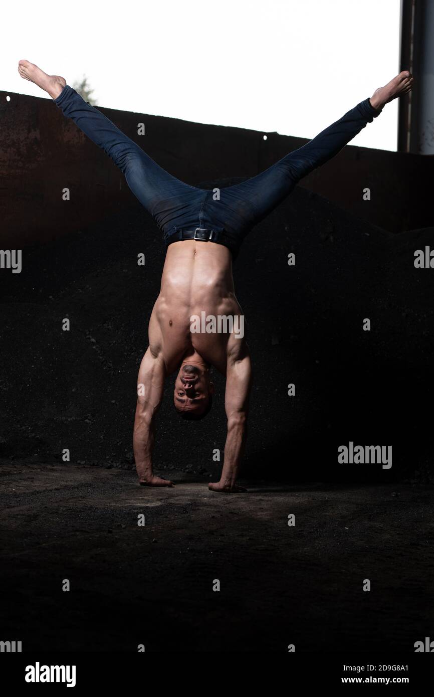 Handsome Man Keeping Balance on Hands in Warehouse - Muscular Athletic Bodybuilder Fitness Model Doing Handstand Push-up Stock Photo