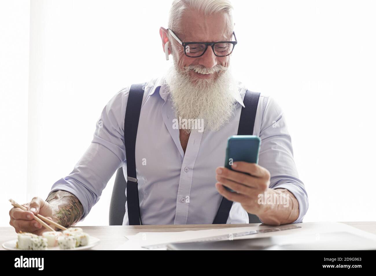 Businessman eating sushi at lunch and looking smartphone.  Entrepreneur inside home studio. Job and modern concept. Stock Photo