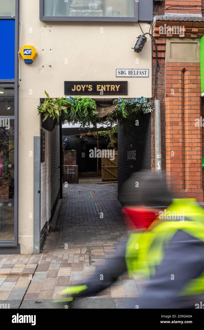 Belfast, Northern Ireland, UK, 4 November 2020: Cyclist wearing a mask rides past the Ann Street end of Joy's Entry. Stock Photo