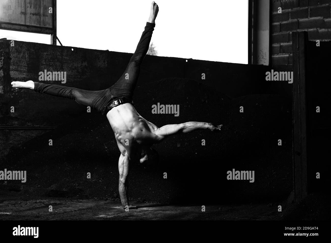 Young Man Keeping Balance on Hand in Warehouse - Muscular Athletic Bodybuilder Fitness Model Doing Handstand Push-up Stock Photo